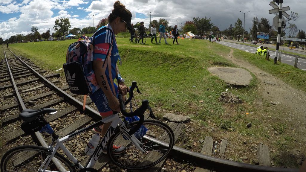 La única descripción es la vida. Mujer ciclista camina al lado de su bicicleta cruzando por la carrilera del tren en un día soleado.